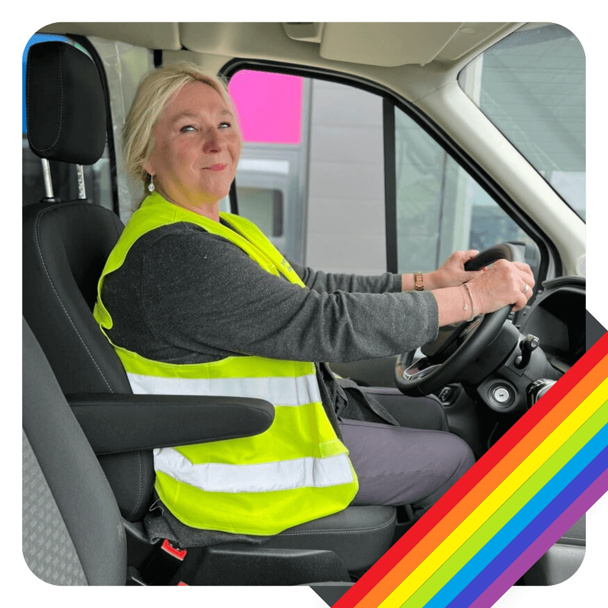 Lächelnde Fahrerin vom Regenbogen Fahrdienst sitzt am Steuer.