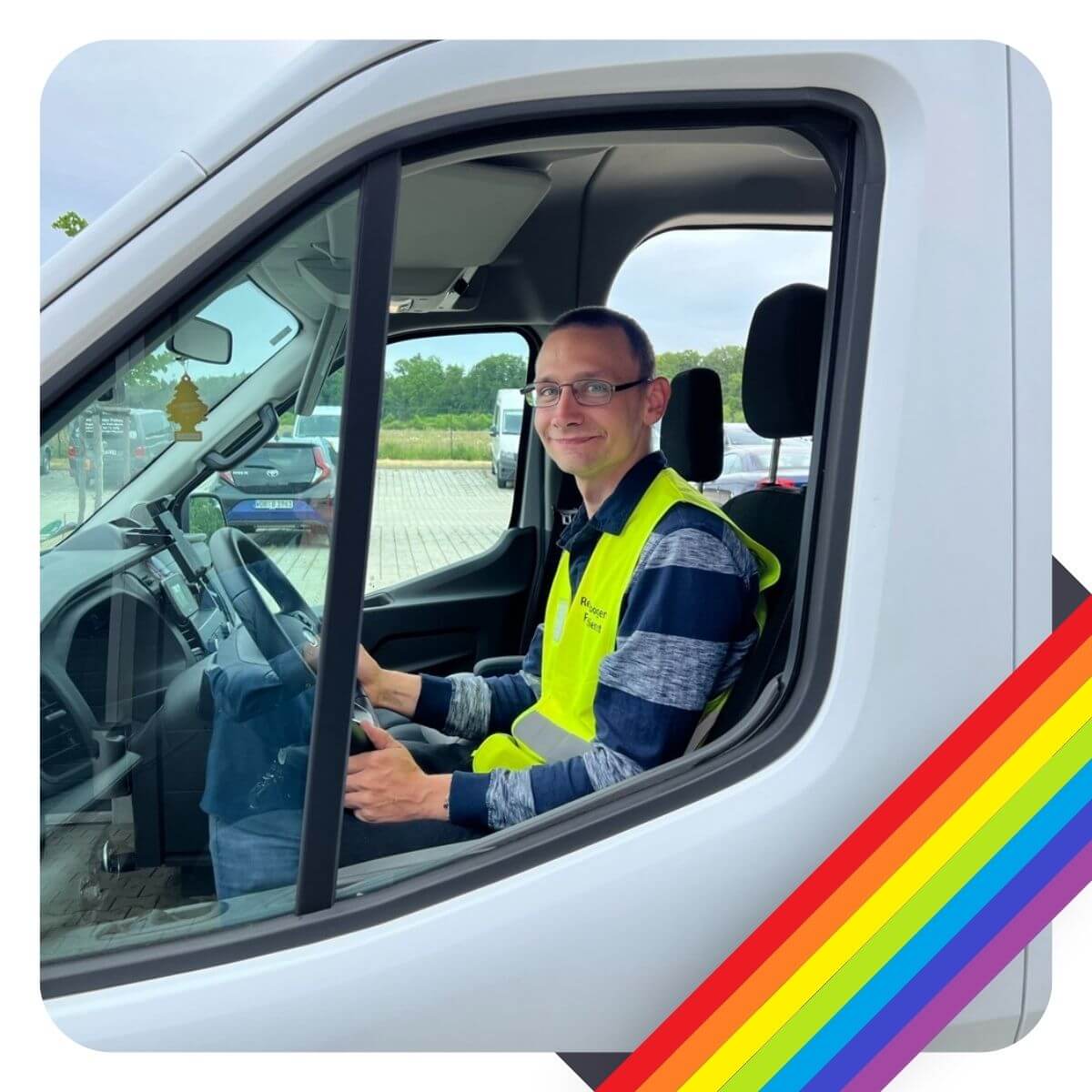 Fahrender vom Fahrdienst Regenbogen sitzt am Lenkrad und lächelt